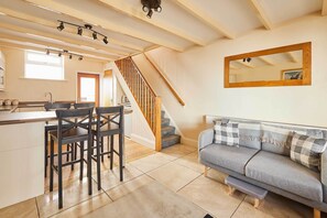 A kitchen with a central island, wooden staircase, and a grey sofa with a mirror above it. - Host & Stay | Sea Haven (Staithes)