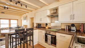 A modern kitchen with white cabinets, stainless steel appliances, and a wooden dining table with chairs. - Host & Stay | Sea Haven (Staithes)