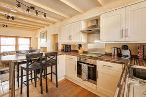 A modern kitchen with white cabinets, stainless steel appliances, and a wooden dining table with chairs. - Host & Stay | Sea Haven (Staithes)