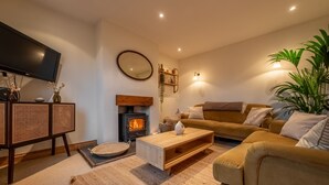 A cozy living room with a fireplace, a flat-screen TV, a sofa, and a coffee table. - Maurice Cottage, Docking, Norfolk (Docking)
