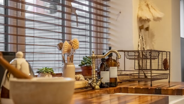 A kitchen counter with a wooden surface, a white bowl, a small potted plant, a bottle of hand soap, and a metal rack with a hanging pot. - Maurice Cottage, Docking, Norfolk (Docking)