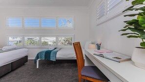 Een hotelkamer met een bed, een bureau, een stoel, een potplant en een raam met jaloezieën.