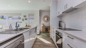 Een moderne keuken met witte kastjes, een Bosch vaatwasser, en een eethoek met houten meubels en uitzicht.