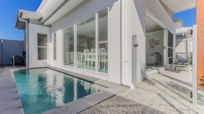A modern house with a swimming pool, large glass doors, and outdoor seating. - Sea Poppy (Casuarina)
