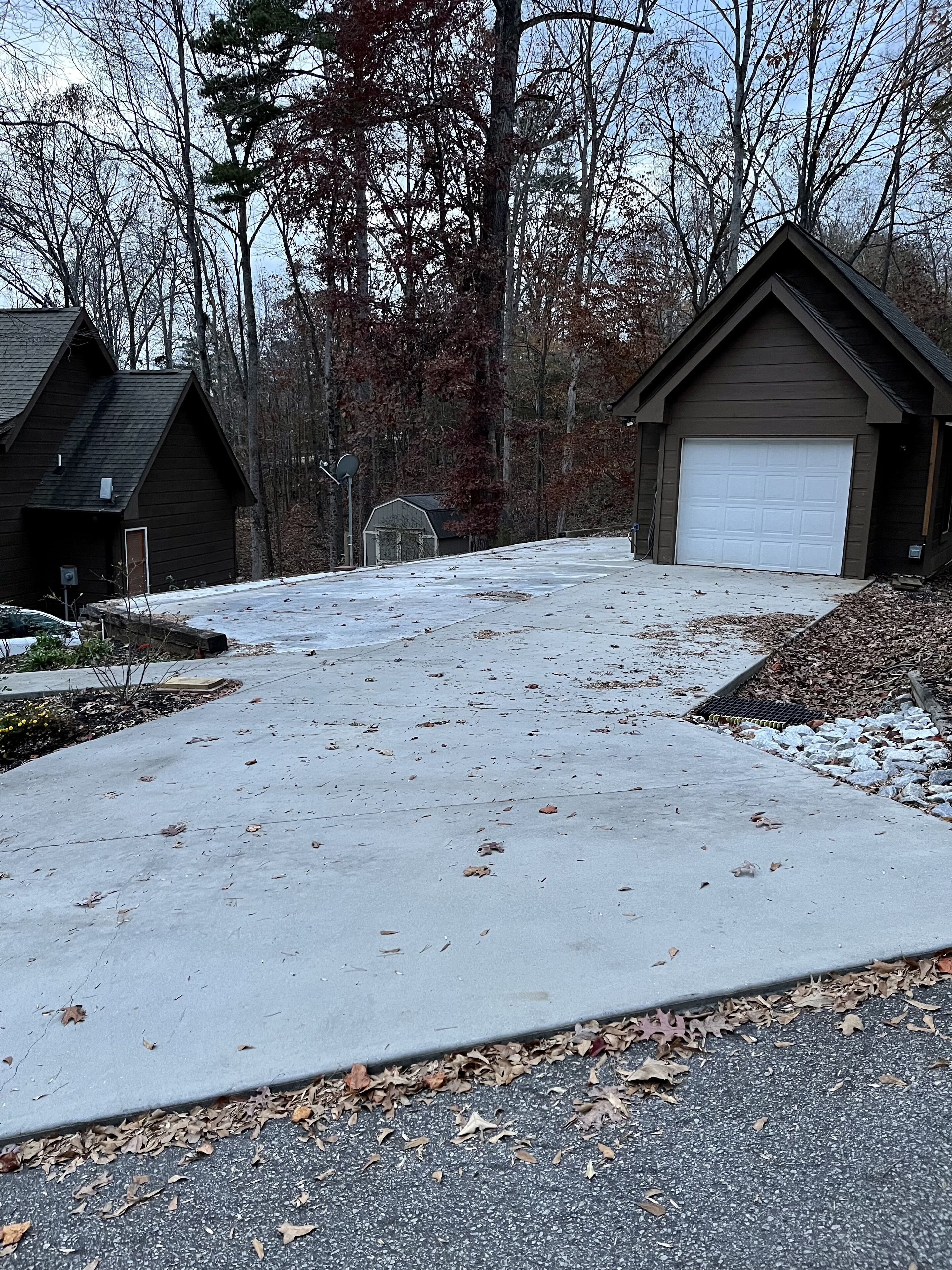 A residential driveway with a garage, a basketball hoop, and a small shed.