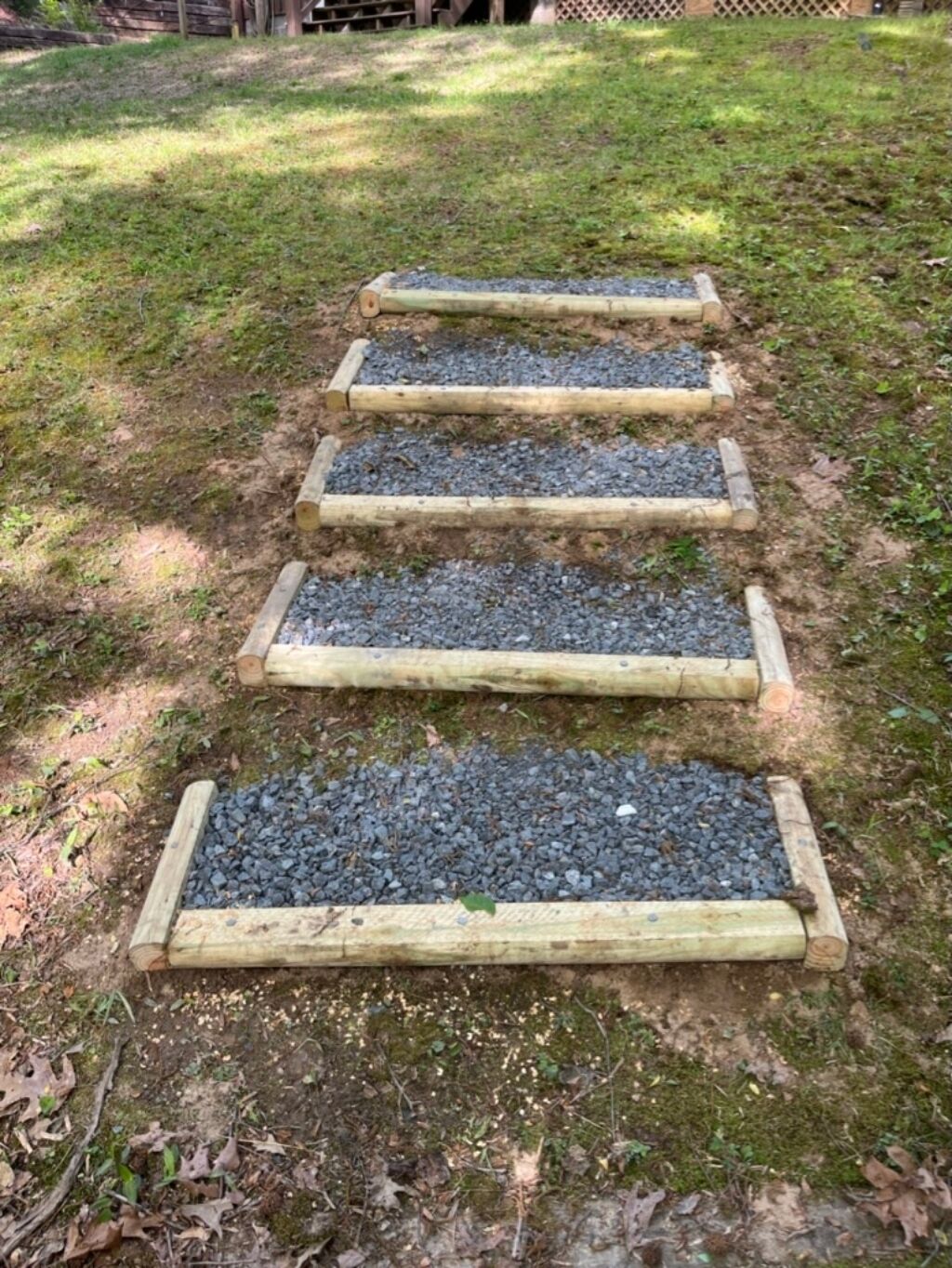 Una escalera de madera con peldaños de grava que asciende por una pendiente cubierta de hierba.