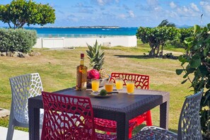 An outdoor dining area with a table set for two, featuring a bottle of liquor, a pineapple, and glasses of orange juice.