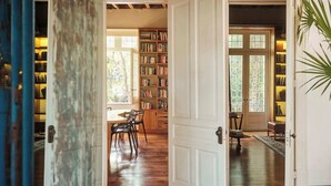 A spacious room with a wooden floor, a large open door leading to a library filled with bookshelves, and a dining area with chairs and a table. - Casa Wynwood in Roma Norte (Ciudad de México)