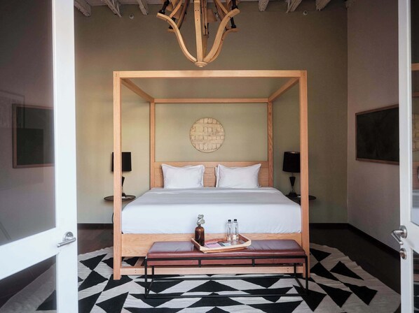 A four-poster bed with a wooden frame, white bedding, and a round wall clock.