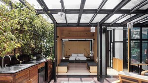 A modern kitchen with a wooden countertop and sink, a glass-enclosed sleeping area with a bed and bench, and a wooden deck with a glass door leading to the sleeping area. - Casa Wynwood in Roma Norte (Ciudad de México)