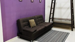 A modern living room with a dark brown sofa, a patterned pillow, and a black and white striped rug. There are three framed artworks on the purple wall and a black ladder leaning against the wall. - Charming studio with a nice pool (Playa del Carmen)