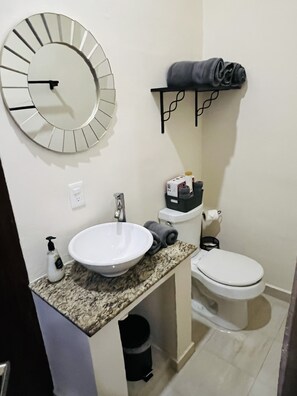 Un baño con un espejo redondo, un lavabo, un inodoro y un perchero para toallas.
