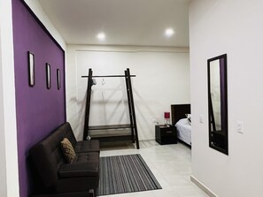 Un dormitorio moderno con una barra de dominadas, un sofá negro con un cojín estampado, una mesita de noche con una lámpara y un espejo grande en la pared.