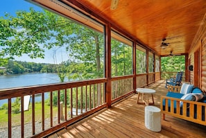 A wooden deck with a view of a lake, a sofa, and a small table. - Waterfront Log Cabin w/Hot Tub, Kayaks, Firepit, King Beds, & Pets OK (Catawba)