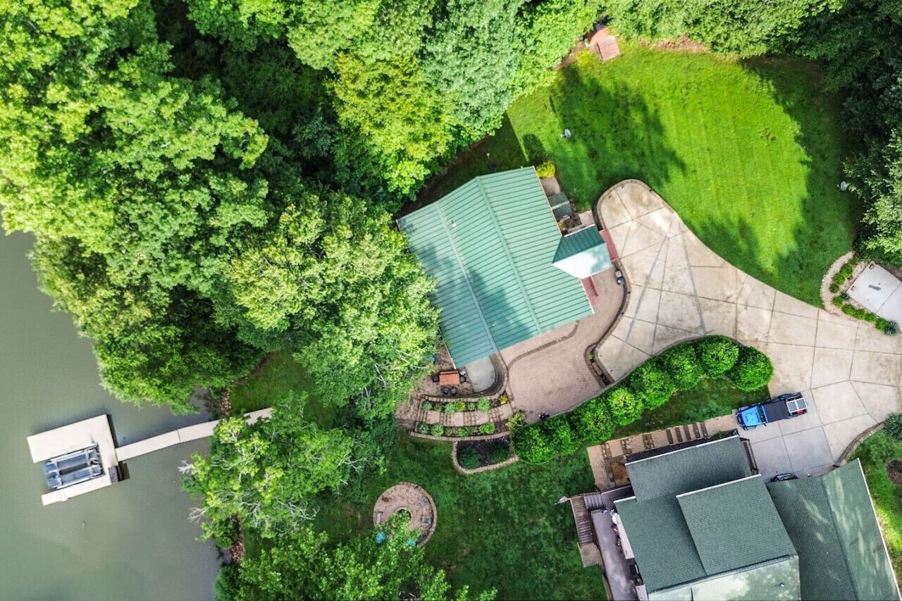 An aerial view of a house with a green roof, surrounded by lush greenery and a dock extending into a body of water.
