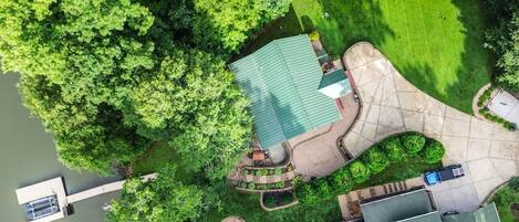 An aerial view of a house with a green roof, surrounded by lush greenery and a dock extending into a body of water.