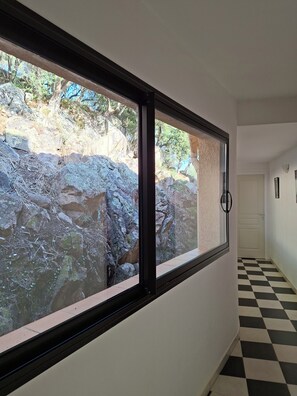A hallway with a checkered floor, a door, and a window overlooking a rocky outdoor area.