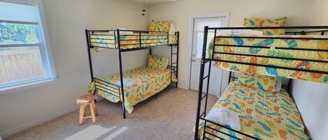 A dormitory room with bunk beds, a ceiling fan, a window, and a small stool.