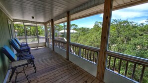 A covered porch with wooden flooring, a railing, and a row of blue chairs. - Easy Beach Access - Short 2 block walk to the beach! (St. George Island)