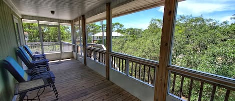 A covered porch with wooden flooring, a railing, and a row of blue chairs.