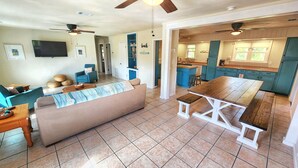 A spacious living area with a sofa, coffee table, and a dining table. There is a kitchen area with blue cabinets and a countertop. - Easy Beach Access - Short 2 block walk to the beach! (St. George Island)
