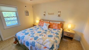 A bedroom with a bed, two bedside tables, a window, and a wall decoration. - Easy Beach Access - Short 2 block walk to the beach! (St. George Island)
