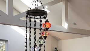 Een kroonluchter met meerdere hanglampen in een kamer met een standbeeld op een plank en een raam met uitzicht op bomen.
