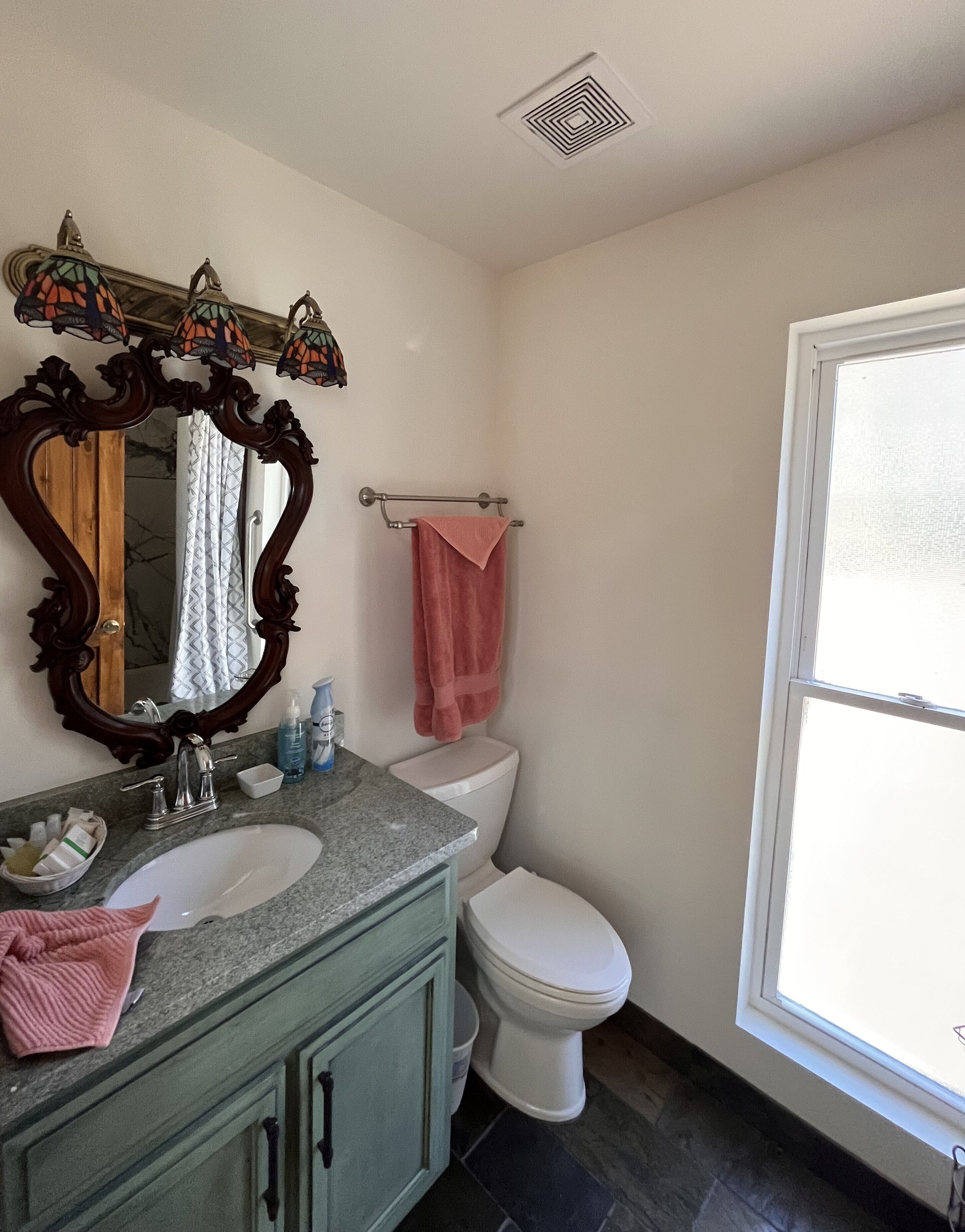 Une salle de bain avec un lavabo en marbre, un grand miroir, des toilettes et une fenêtre.