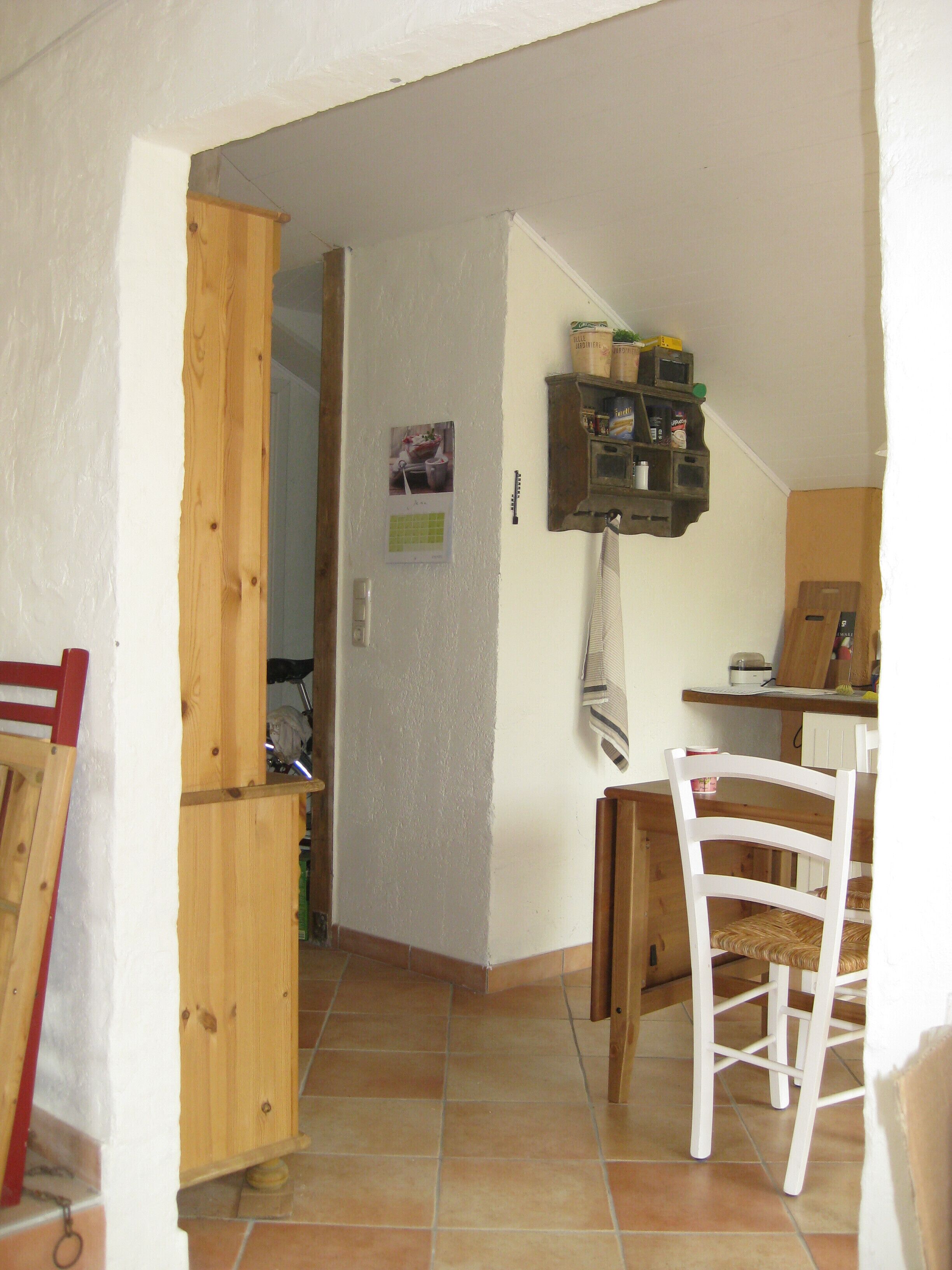 Eine Küche mit einem Holzkasten, einem weißen Stuhl und einem Fliesenboden.