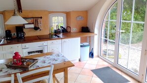 Une cuisine dotée d’un plan de travail en bois, de meubles blancs, d’une table à manger avec des chaises, d’une lanterne rouge et d’une fenêtre donnant sur un paysage verdoyant.