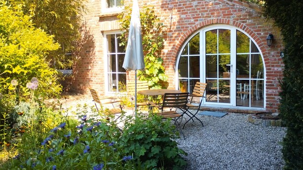 Un bâtiment en briques doté d’une grande fenêtre en arc de cercle et d’un patio avec une table et des chaises.
