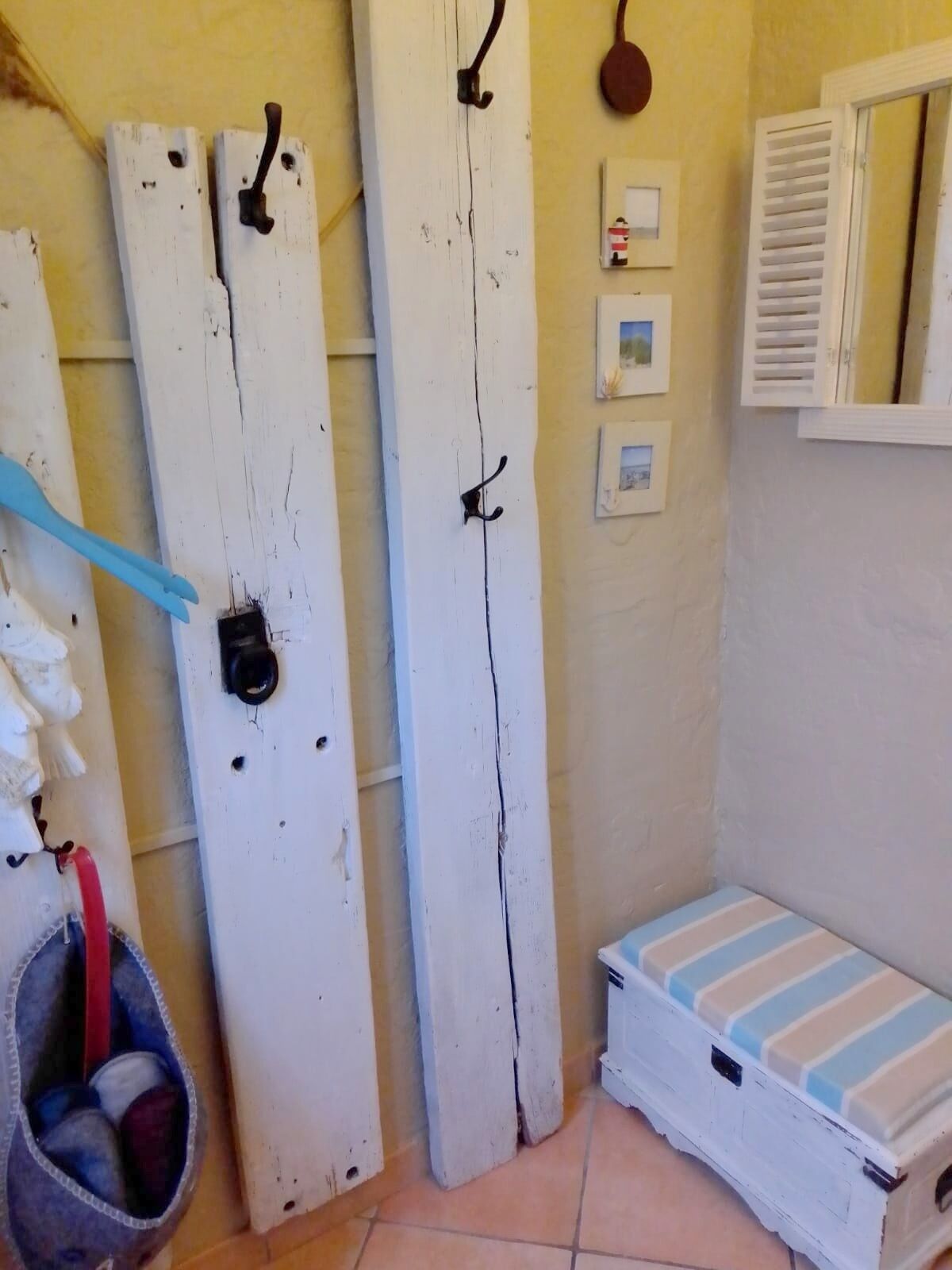 Une petite pièce, de taille modeste, avec une porte blanche, une petite fenêtre avec des volets, un tableau accroché au mur et un petit lit avec une literie à rayures.
