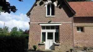 A brick house with a white door and window, surrounded by greenery.