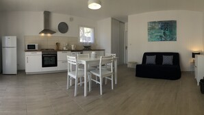 Une cuisine moderne avec des meubles blancs, un coin repas avec des chaises blanches et un canapé noir.