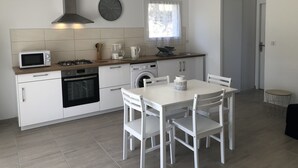 Une cuisine moderne avec des meubles blancs, un four à micro-ondes, une cuisinière et un évier. On y trouve une table à manger avec des chaises et une fenêtre avec des rideaux.