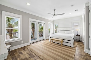 Une chambre Ă coucher comprenant un lit, un ventilateur de plafond, une fenĂȘtre avec des stores et une porte donnant sur un balcon.