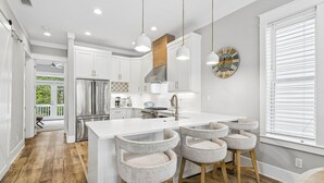 A modern kitchen with white cabinetry, a central island, pendant lighting, and a large window with blinds. - Coastal Pet-Friendly Home w/ Brand New 1st Floor Deck | Near Lagoon Pool & Beach (Panama City Beach)