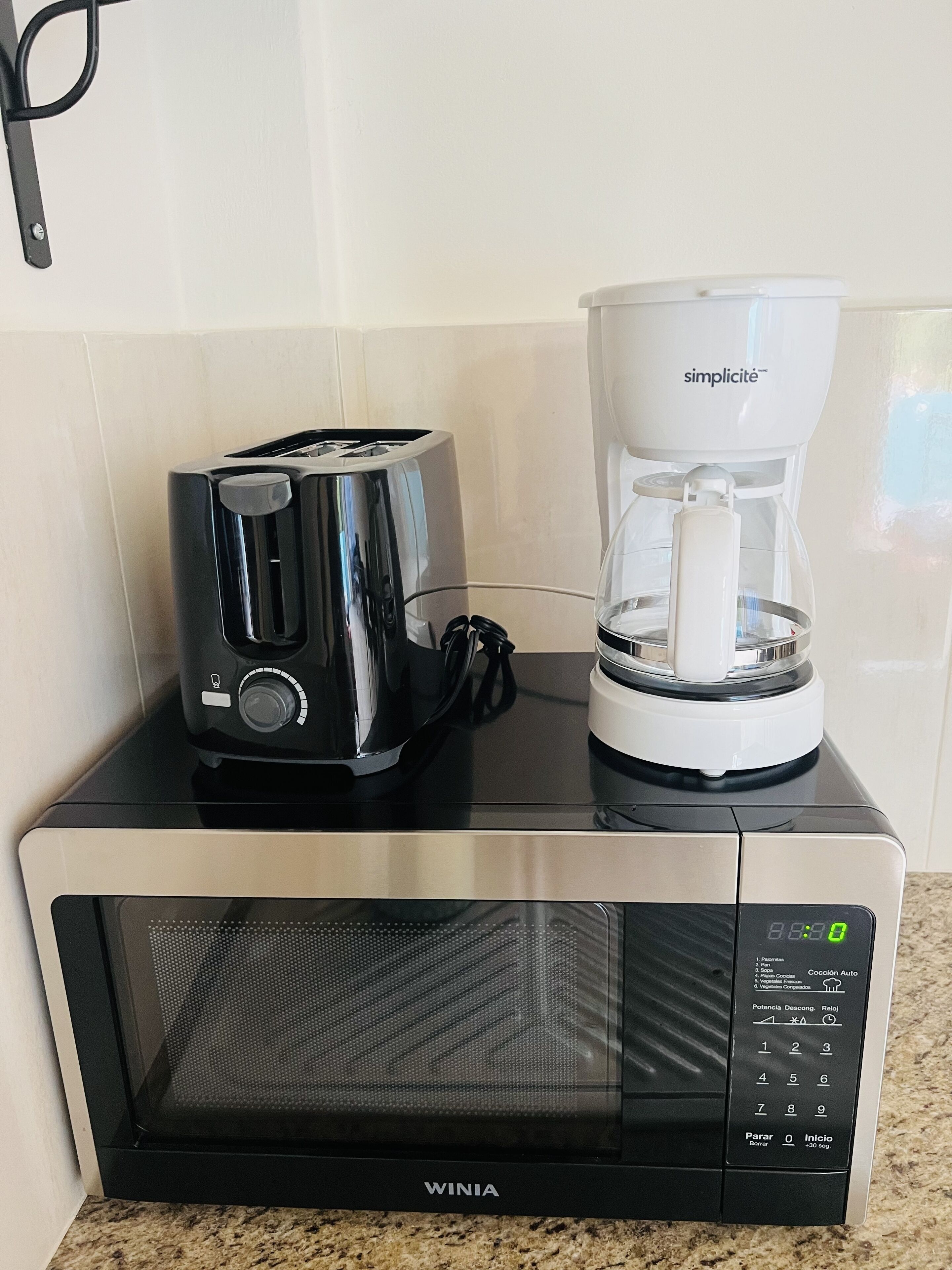 Eine Küche mit einer schwarzen Mikrowelle, einem schwarzen Toaster und einer weißen Kaffeemaschine, die auf der Mikrowelle steht.