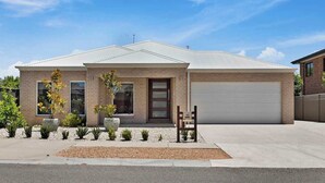A two-story house with a garage, a front porch with a chair, and a driveway. - The Witton Yarrawonga - Spring Offer (Yarrawonga)