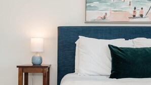 Un letto con cuscini bianchi e verde scuro, una testiera blu e un comodino con una lampada.