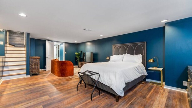 Quarto moderno com uma cama grande, piso de madeira e parede azul de destaque.