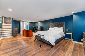 A modern bedroom with a large bed, wooden flooring, and a blue accent wall. - Cozy, Affordable, Luxurious | Central Location (Indianapolis)