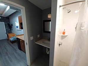 Une petite salle de bain comprenant une douche, un lavabo et une petite étagère où sont rangés les articles de toilette.