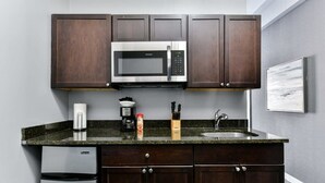 Una cucina compatta con mobili in legno scuro, un forno a microonde in acciaio inox, una macchina da caffè, un lavandino e un piccolo frigorifero.