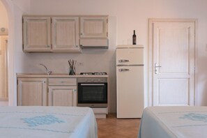 Een kleine keuken met een fornuis, oven en koelkast. Er zijn twee bedden met blauw beddengoed.