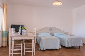 A room with a bed, a desk, a chair, a television, and a table with a bottle and glasses. - Le Residence del Golfo Orosei (Orosei (NU))