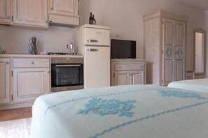 A bedroom with a bed, a television, a kitchenette with a stove, oven, and refrigerator. - Le Residence del Golfo Orosei (Orosei (NU))