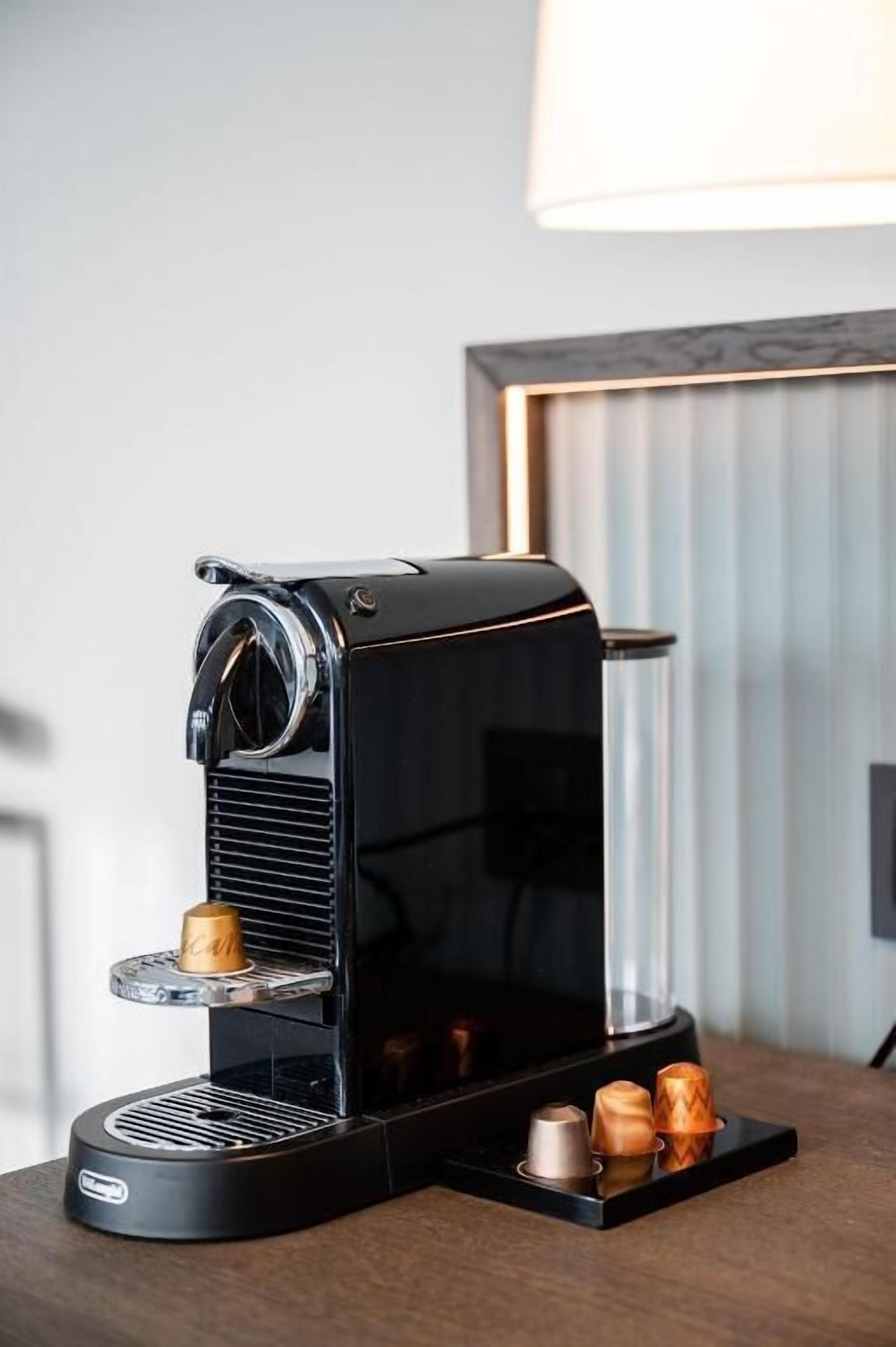 Una máquina de café espresso negra con depósito de agua de vidrio y bandeja metálica para recoger las gotas sobre una mesa.