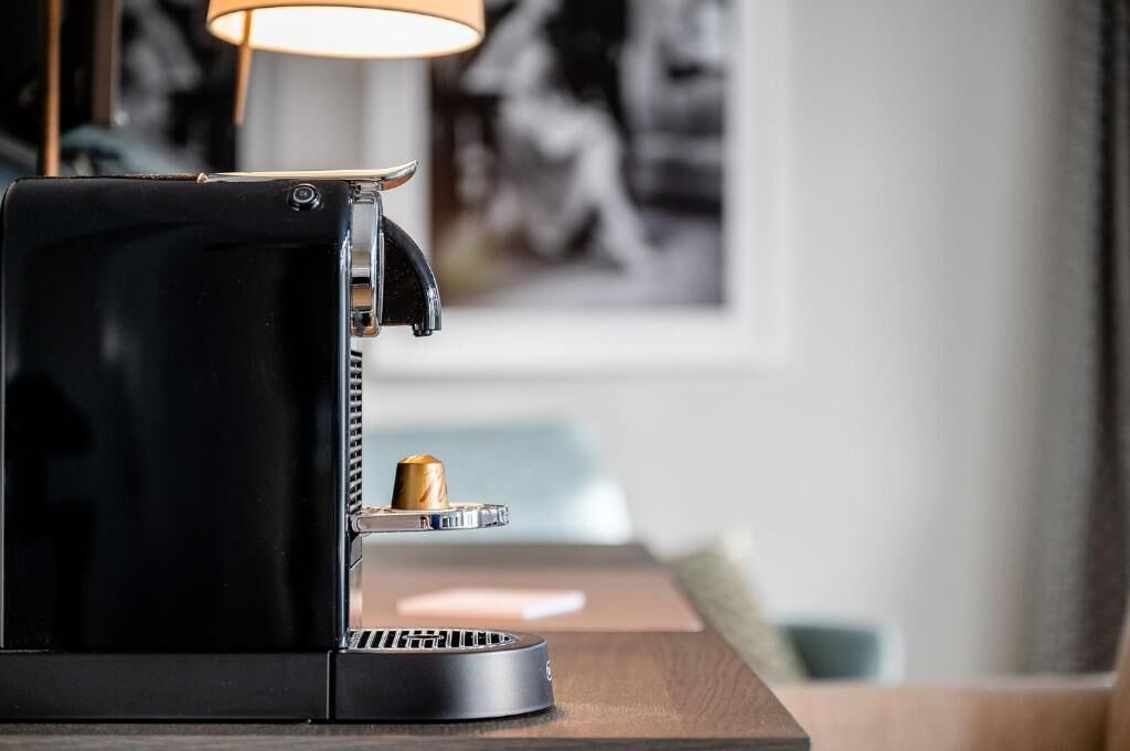 A black espresso machine on a wooden table with a coffee cup on the drip tray.