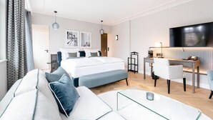 A modern hotel room with a large bed, a sitting area with a glass coffee table, a desk, and a flat-screen TV. - Clounys Hotel & Restaurant (Hamburg)